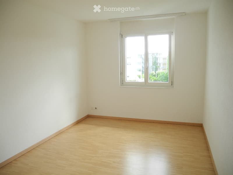 Empty room with light-colored walls, wooden flooring, and a single window with white frame and blinds.