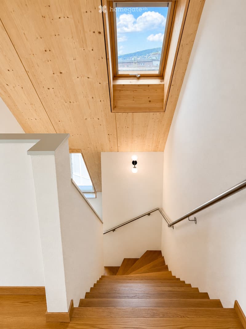 Modern staircase with wooden steps and a metal handrail, featuring a skylight window and recessed lighting.