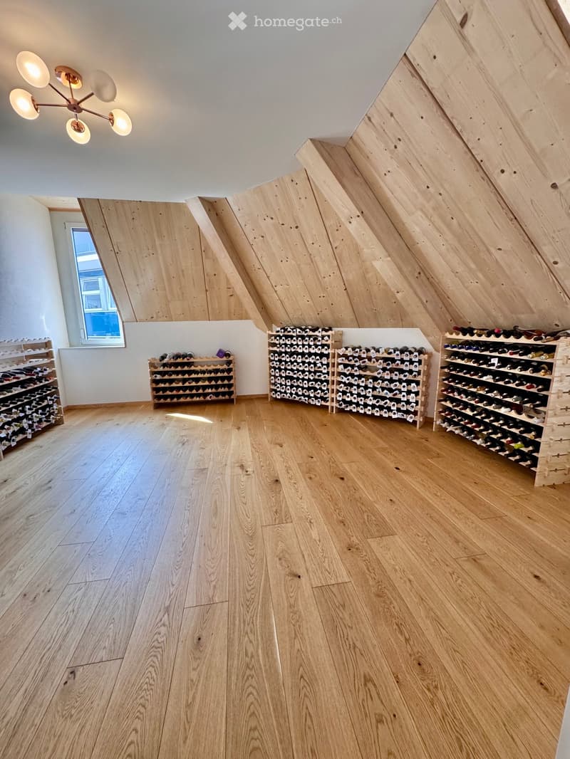 Attic room with wooden floors, slanted wooden ceiling, multiple wine racks, and a chandelier light fixture.