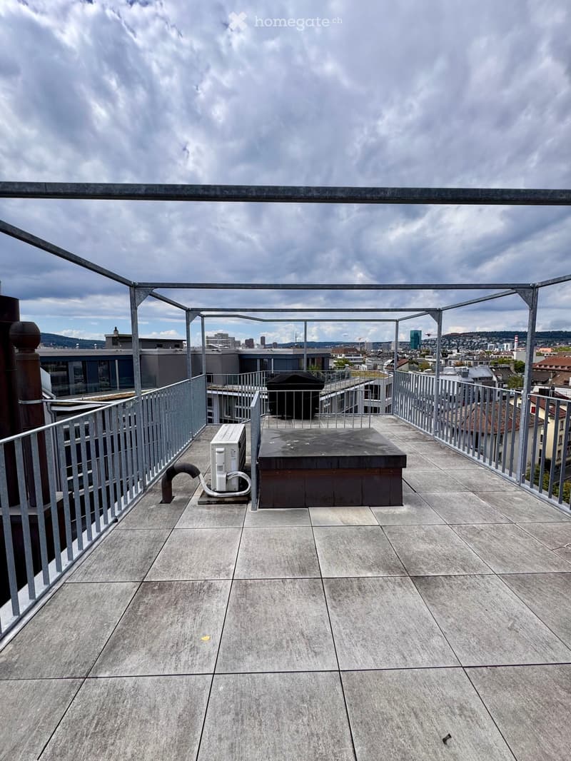Roof terrace with concrete tiles, metal railing, air conditioning unit, and cityscape view.