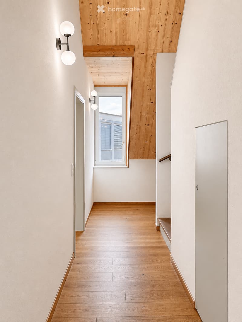 Modern hallway with wooden flooring, white walls, and built-in wooden shelving. Features wall-mounted spherical lights and a window at the end.