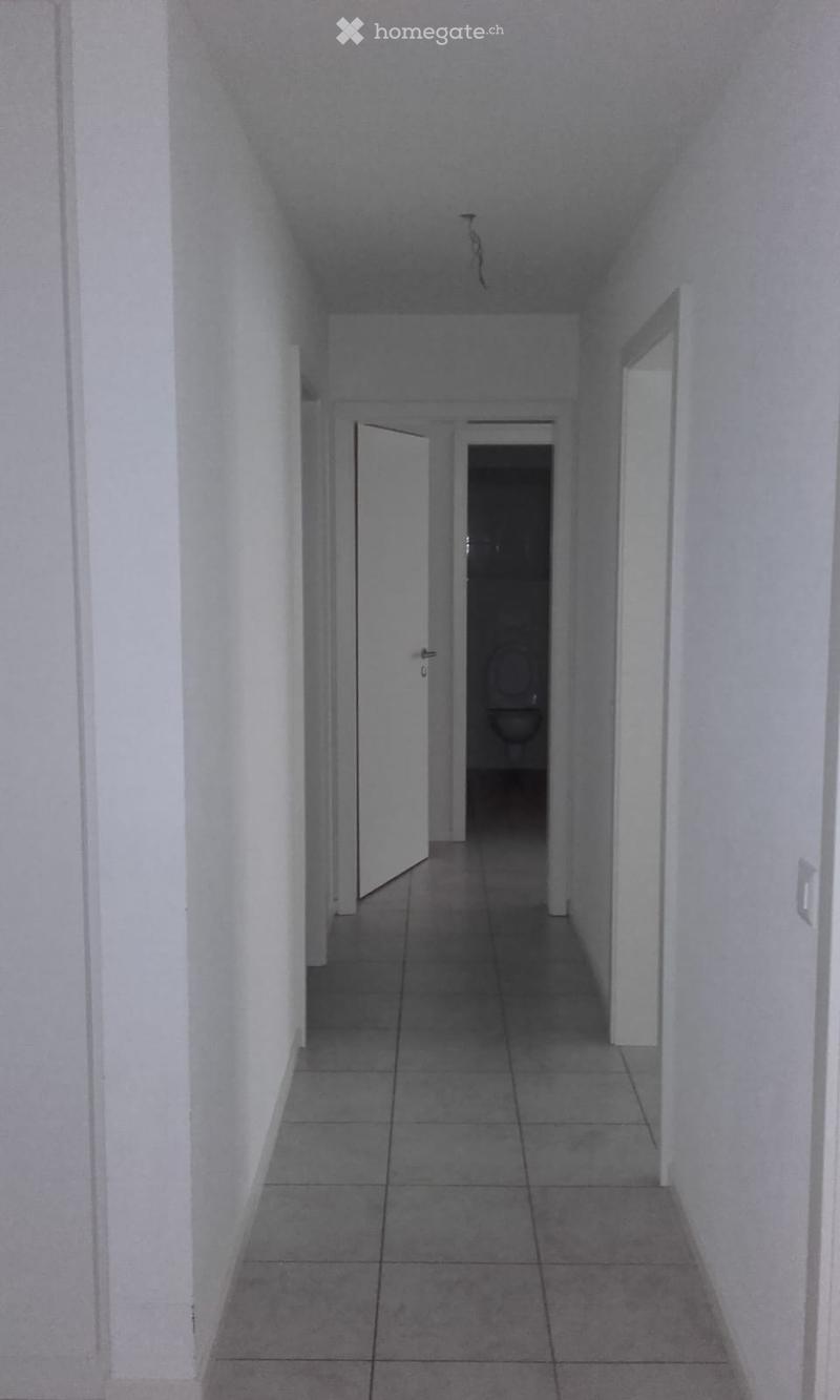Empty hallway with tiled floor, white walls, and a partially open door leading to a bathroom.