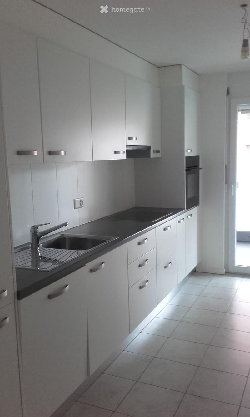 Modern kitchen with white cabinets, stainless steel sink, and built-in oven. The space features tiled flooring and ample natural light from a window.