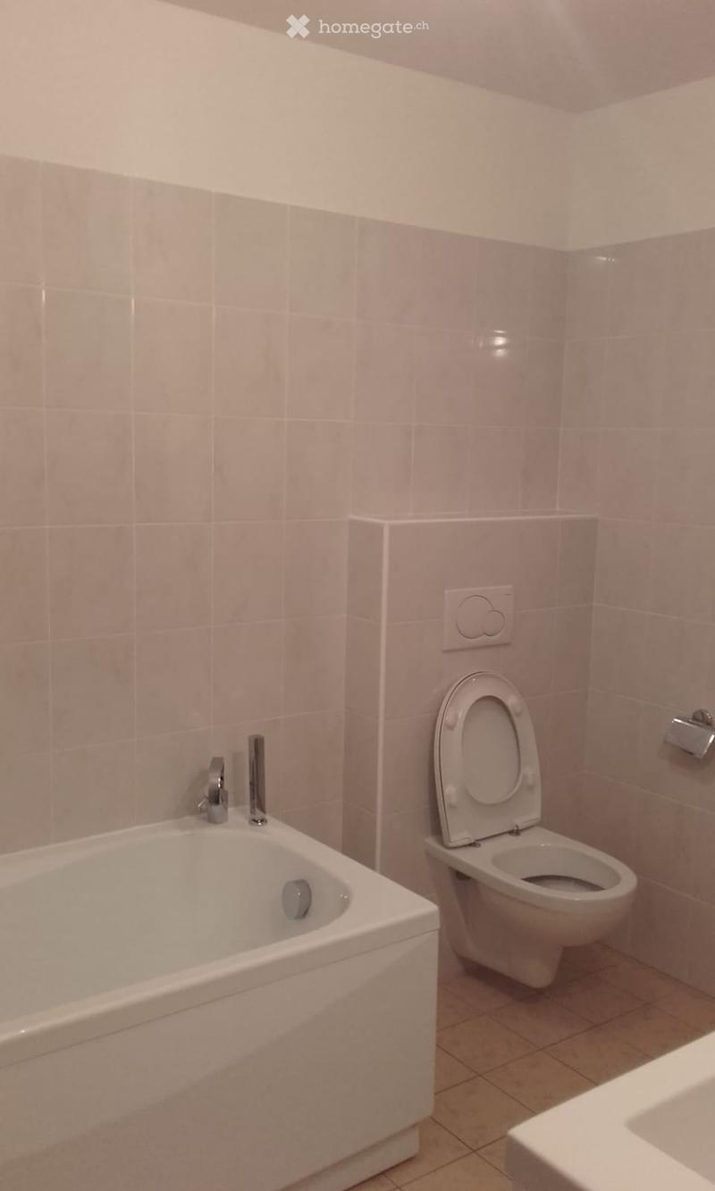 Bathroom with a white bathtub, toilet, and tiled walls.