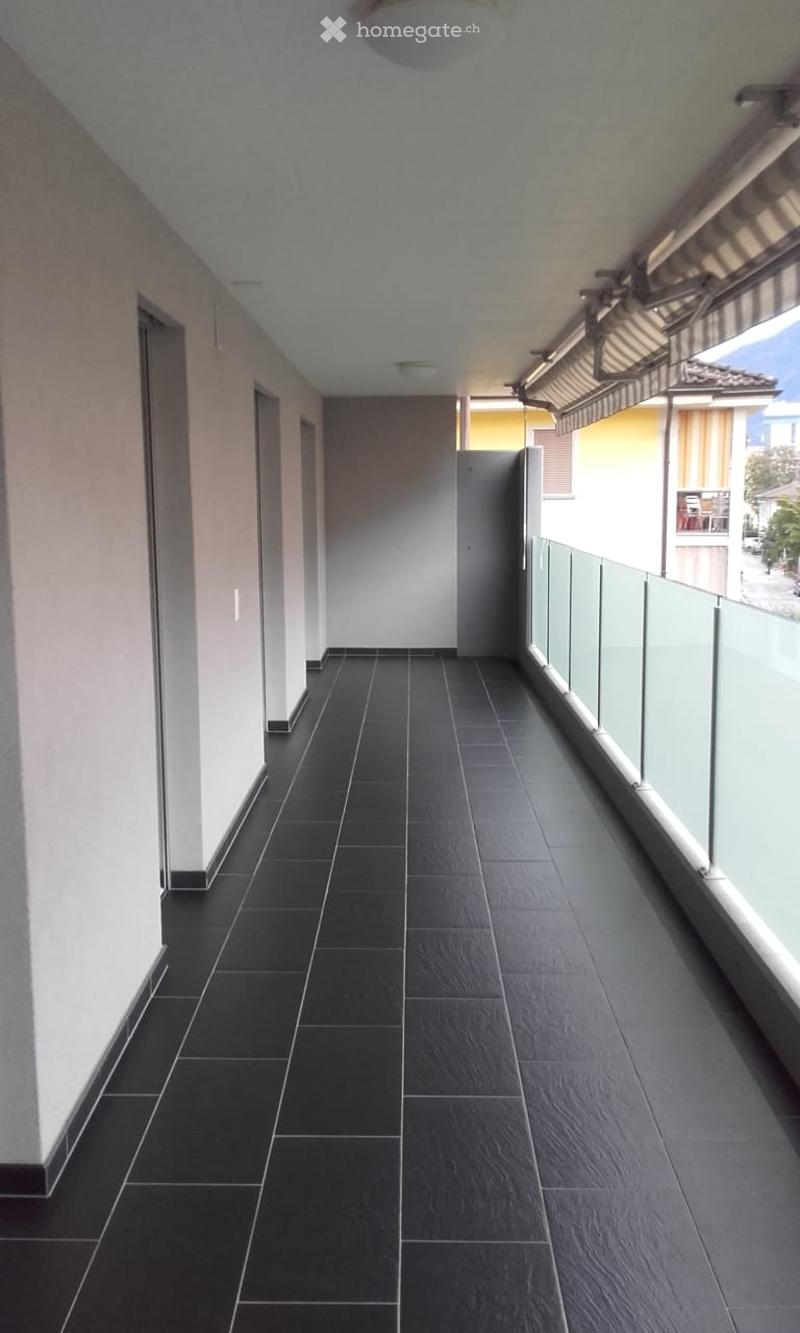 Modern hallway with black tiled flooring, white walls, and glass railings on one side, leading to a door at the end.