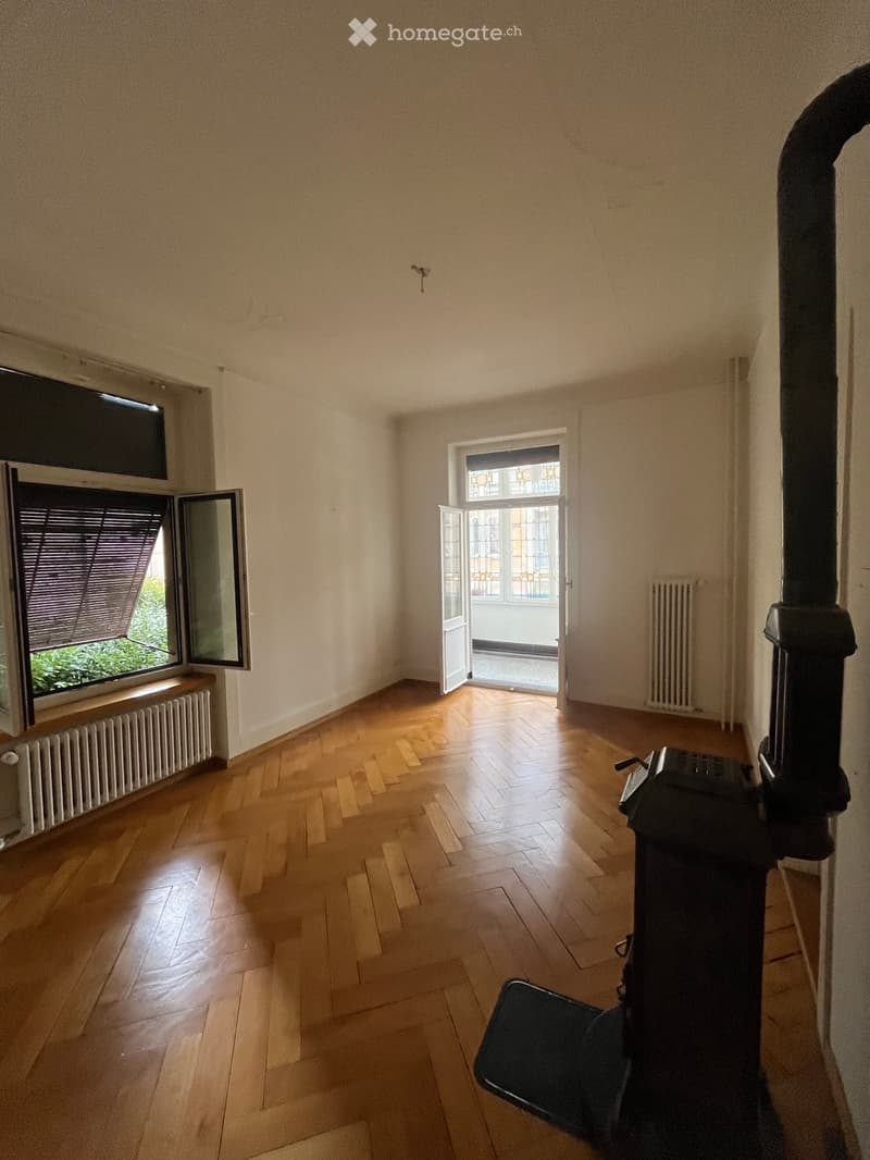 Empty room with wooden flooring, large windows, radiator, and a fireplace with a chimney. No furniture or equipment present.