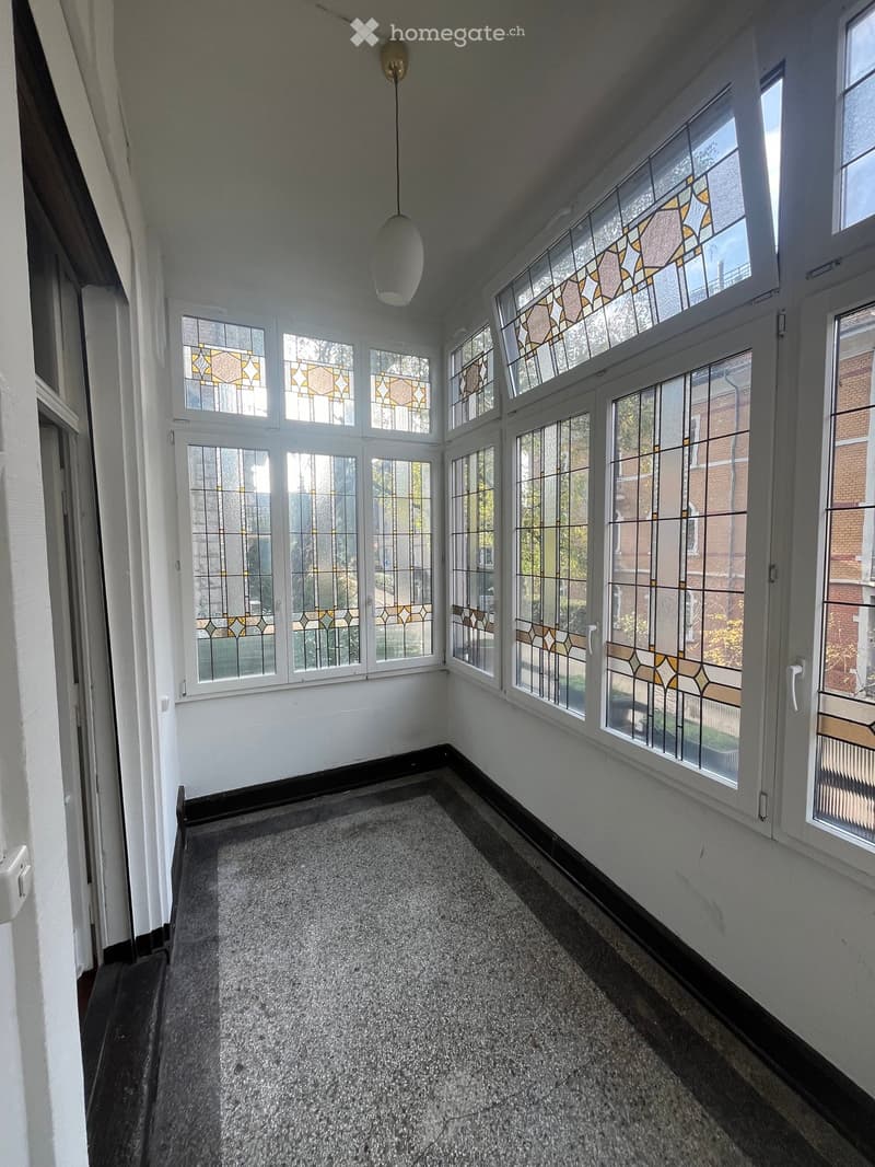 Empty hallway with large windows featuring stained glass, carpeted floor, and a hanging light fixture.