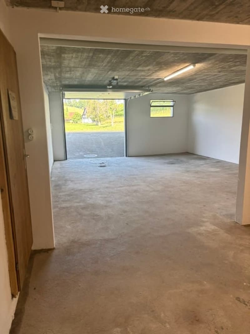Empty garage with concrete floor, white walls, and an open door leading outside. No furniture or equipment present.