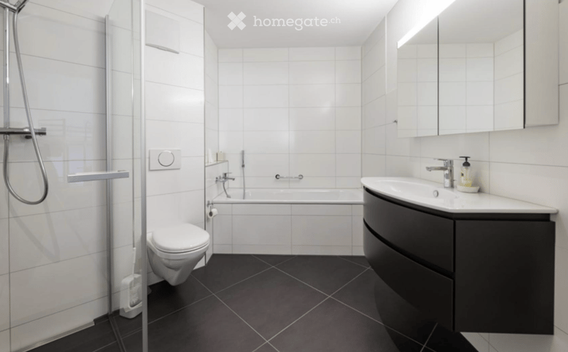 Modern bathroom with white tiled walls, black tiled floor, toilet, bathtub, sink with mirror, and shower area.