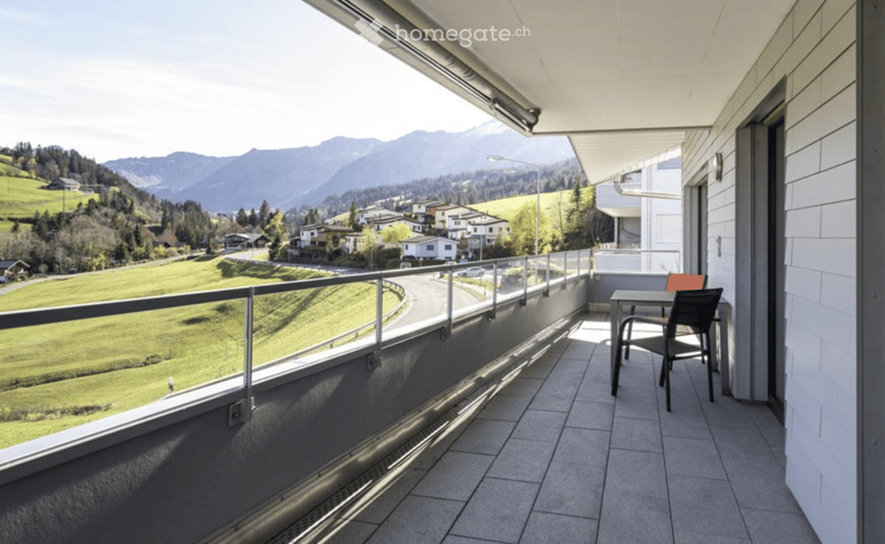 Balcony with tiled floor, metal railing, and scenic mountain view. Includes a small table and chair.