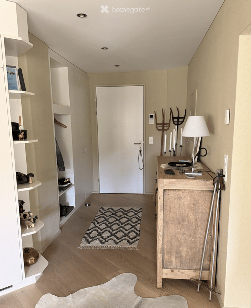 A modern hallway with built-in shelving, a small table with a lamp, and a patterned rug on the floor.
