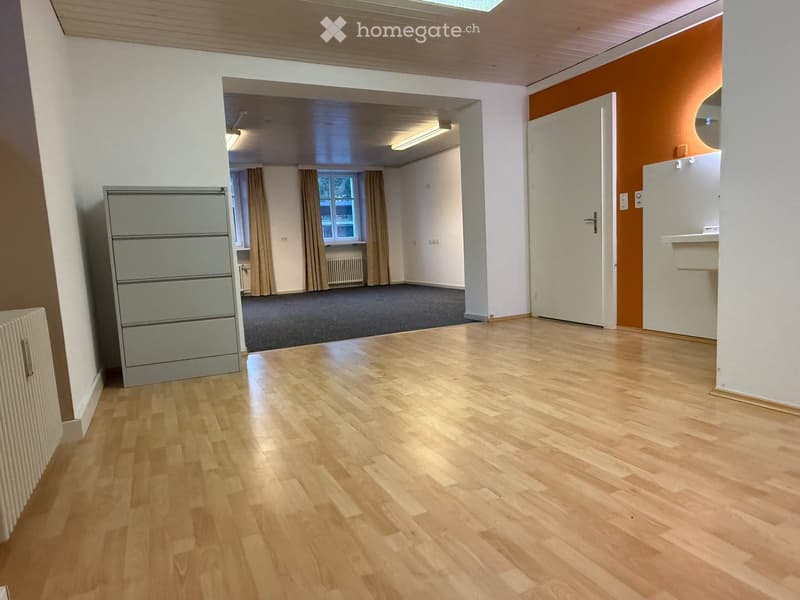Empty room with wooden flooring, white walls, and a grey carpeted area visible in the background. No furniture or equipment present.