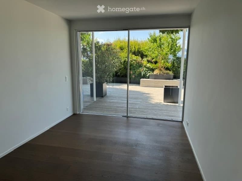 Bright, empty room with wooden flooring and large glass sliding doors leading to a garden area.