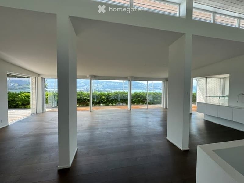 Open-plan unfurnished room with large windows and a view of the landscape, featuring a wooden floor and white walls.