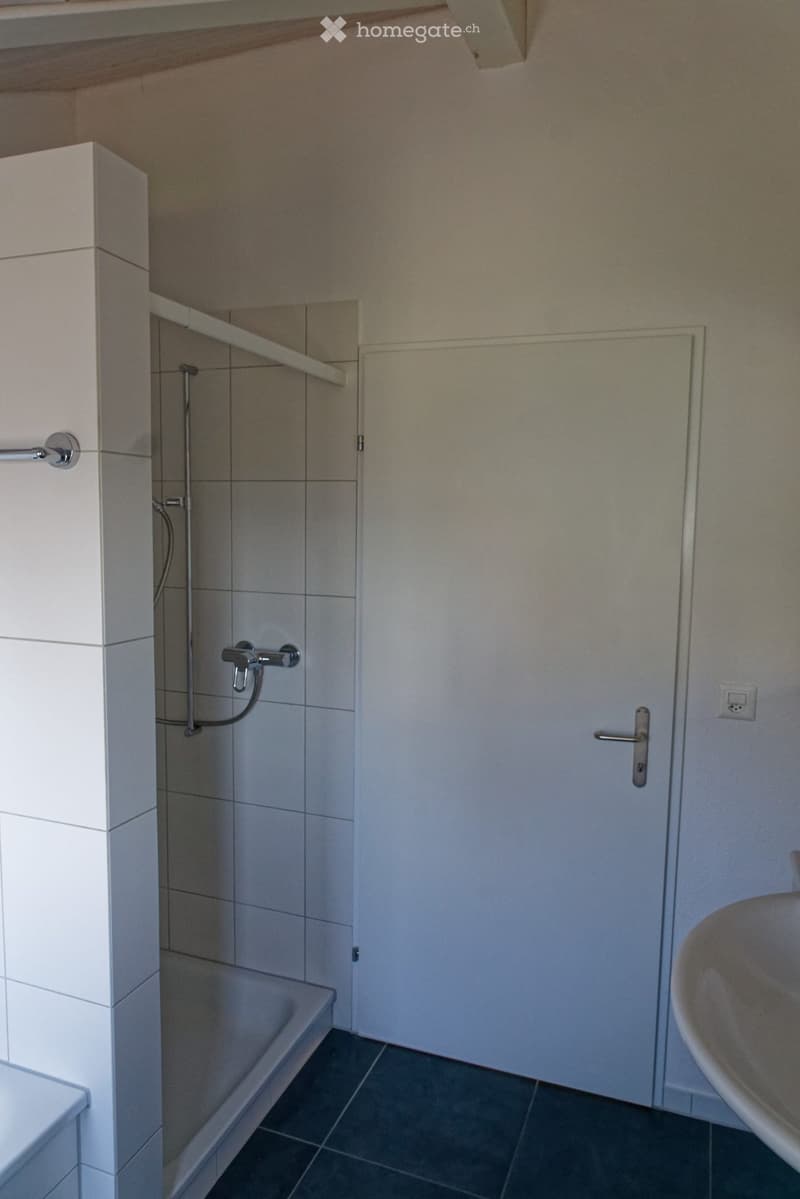 Modern bathroom with a bathtub, tiled walls, a door, and a sink.