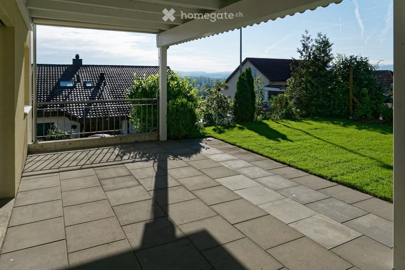 A tiled balcony with a metal railing overlooks a well-maintained lawn and neighboring houses.