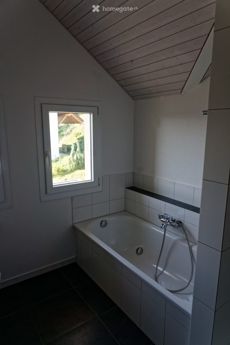 Modern bathroom with a bathtub, tiled walls, and a window offering a view of the garden.
