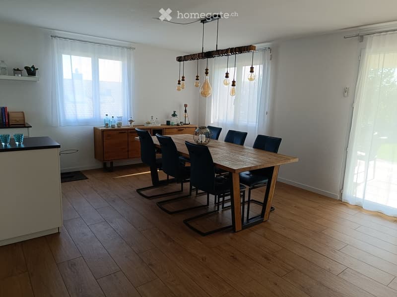 Bright kitchen with wooden flooring, large dining table surrounded by black chairs, wooden cabinetry, and decorative items on the counter.