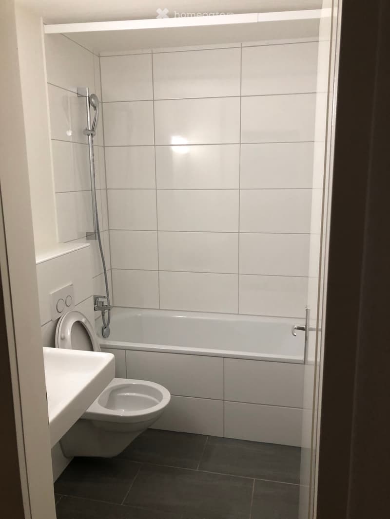Modern bathroom with white tiles, a toilet, a sink, a bathtub, and a showerhead.