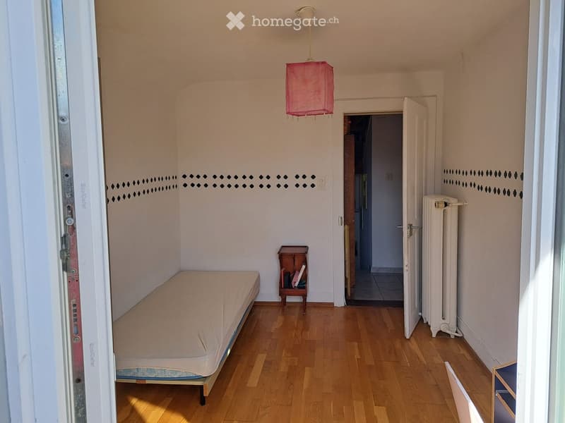 Small bedroom with wooden flooring, a single bed, a nightstand with books, a radiator, and a pink pendant lamp.
