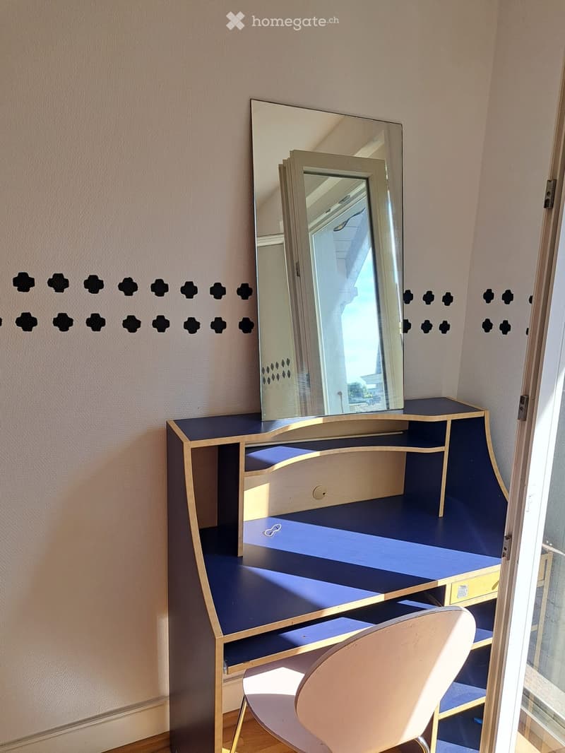 A stylish vanity with a large mirror, blue countertop, and a matching chair in a room with patterned wall design.