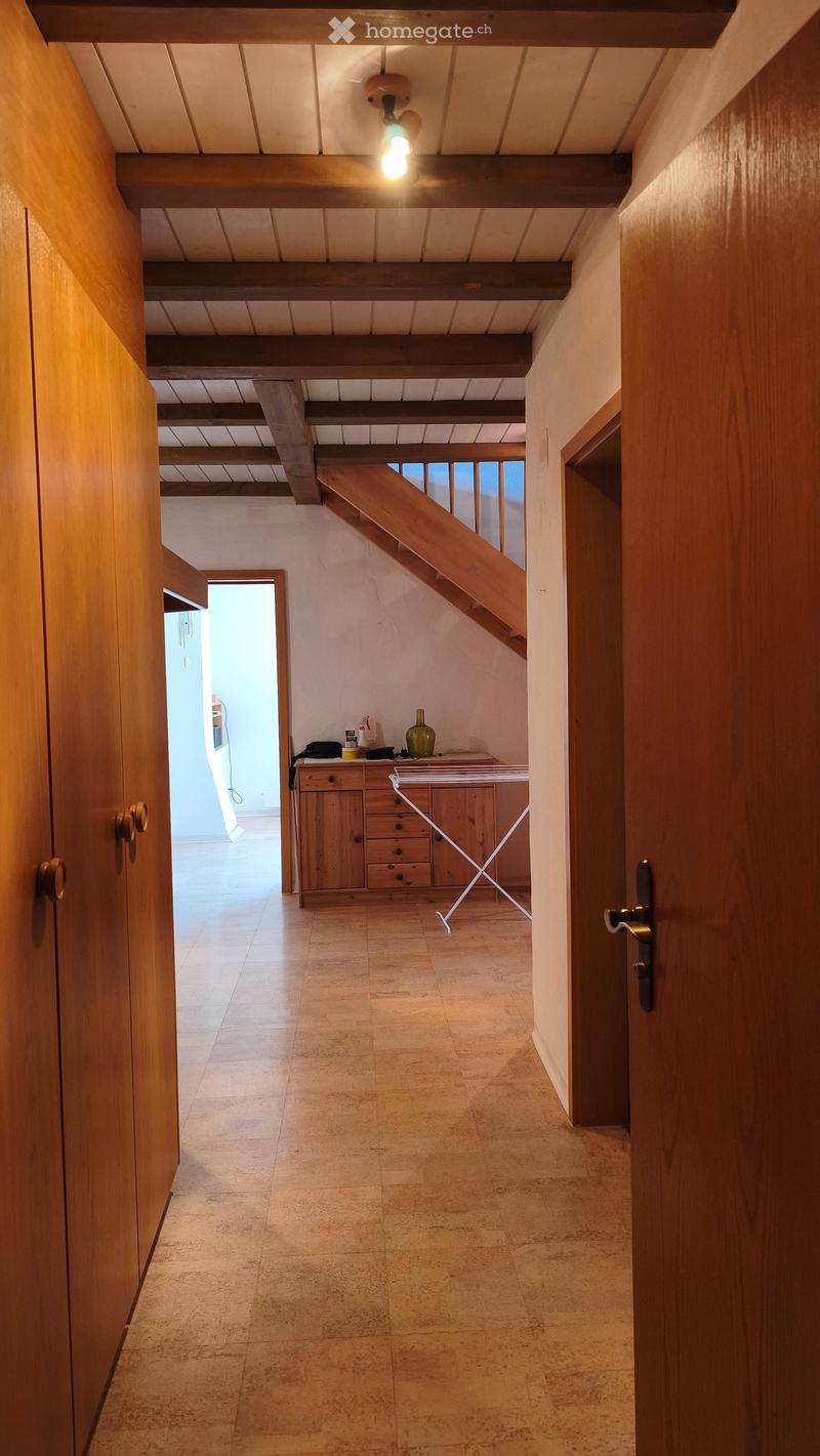 A hallway with wooden doors, a staircase leading upwards, and a small wooden cabinet with drawers and a vase on top.