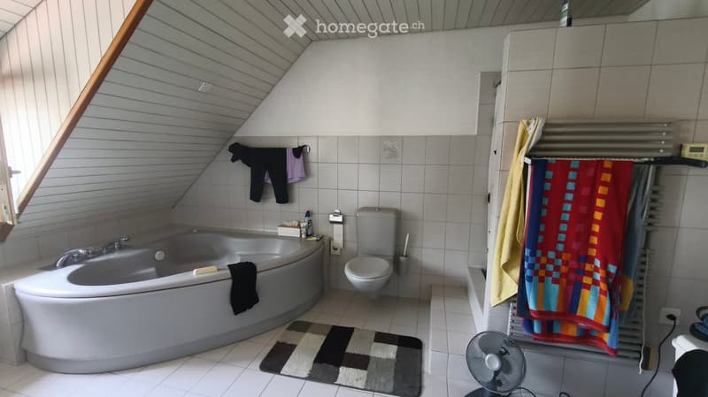Bathroom with a bathtub, toilet, towel rack, and a fan on the floor.