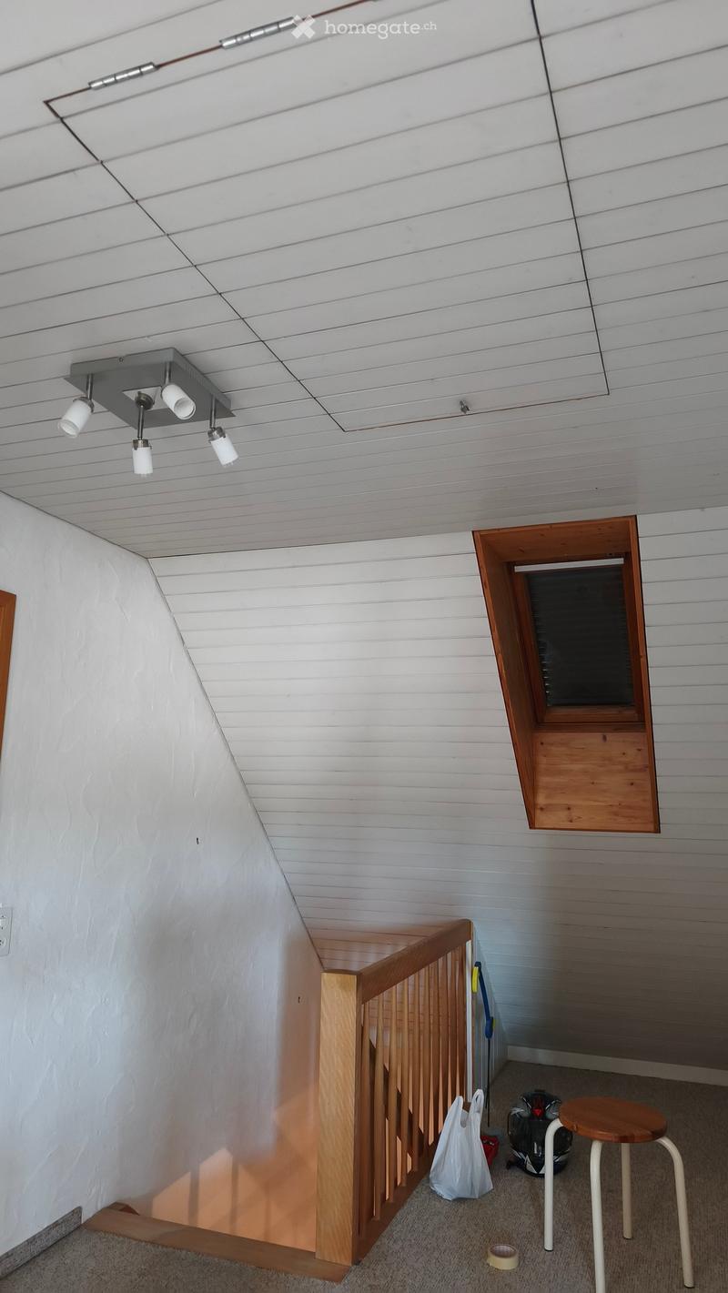 A small, modern hallway with a wooden railing, a small window, and a few items including a stool, a helmet, and a plastic bag on the floor.