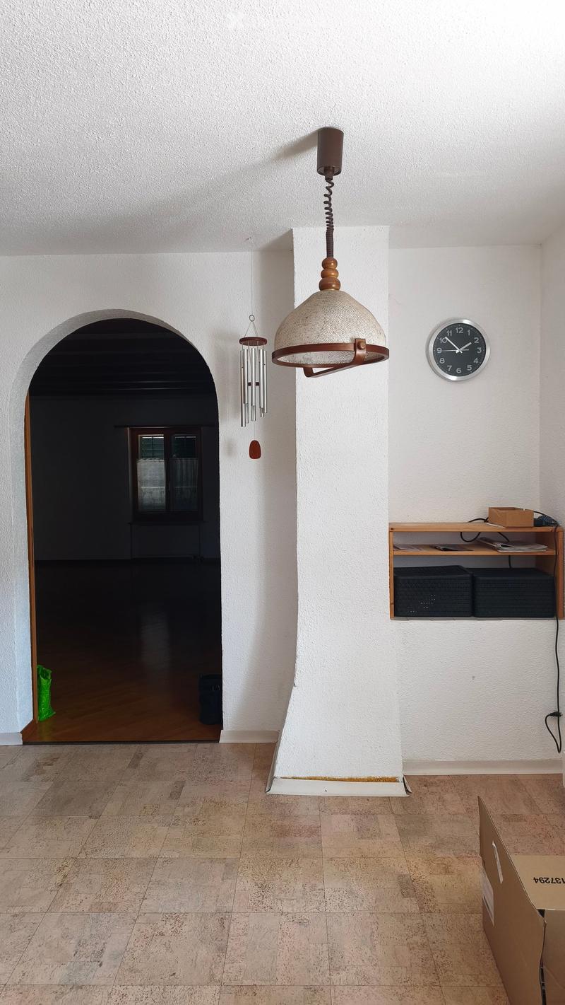 Empty hallway with tiled floor, white walls, a hanging light fixture, a wind chime, a clock, and a small shelf with items on it.