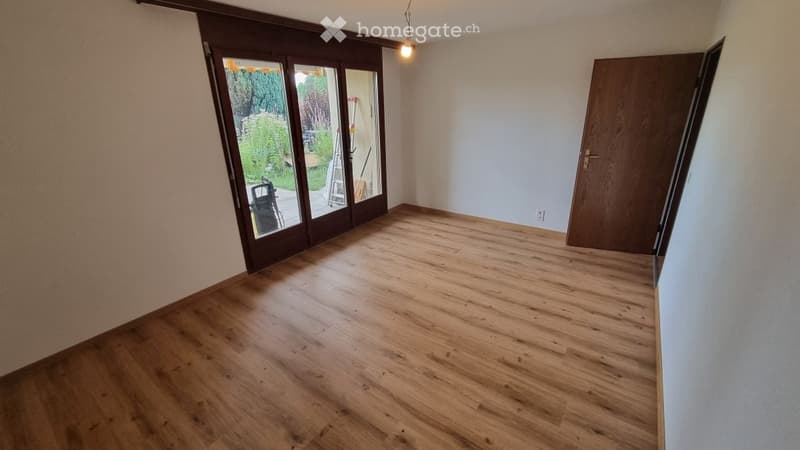 Empty room with wooden flooring, large sliding glass doors leading to an outdoor area, and a closed wooden door.