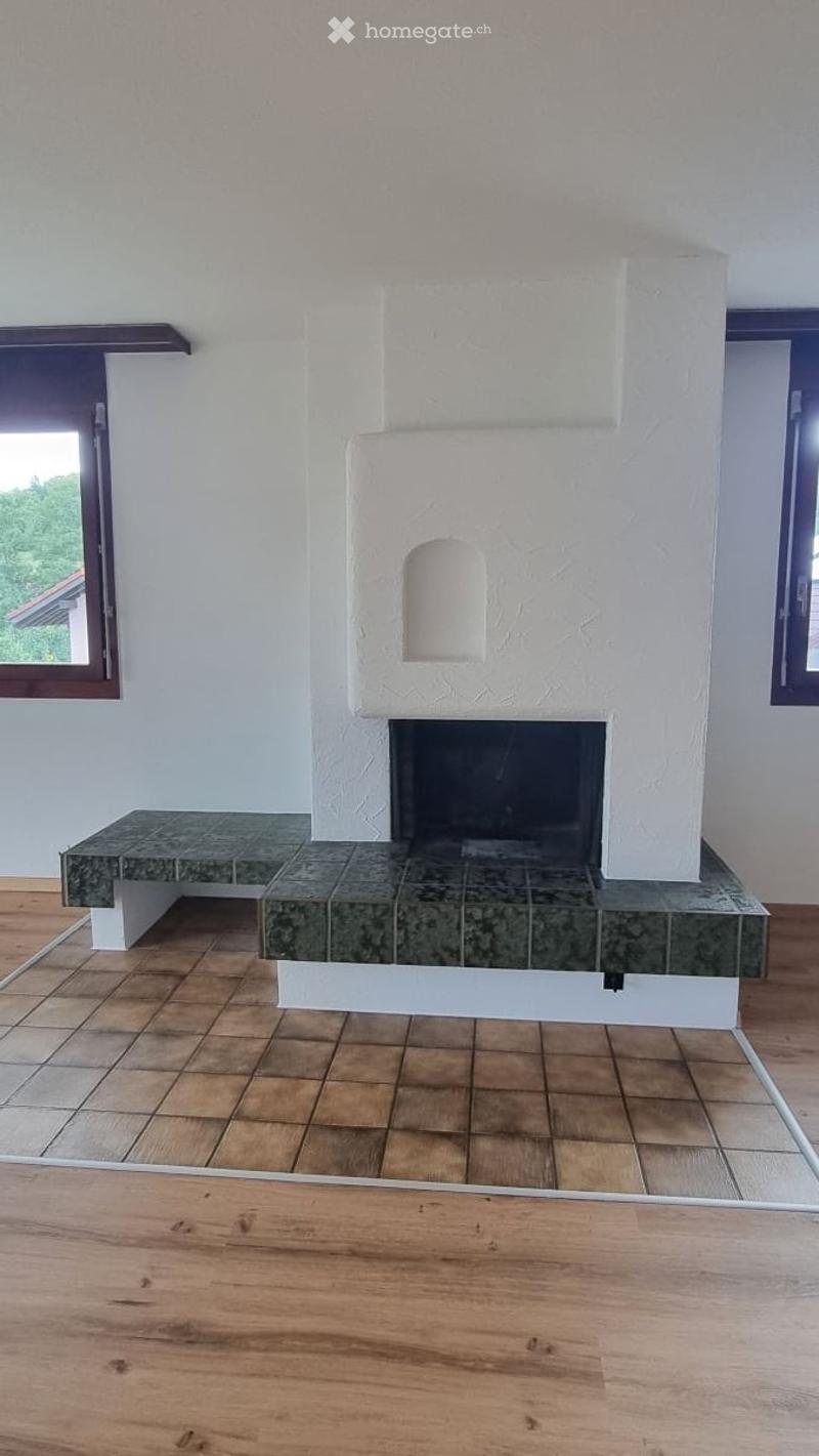 Modern living room with a white fireplace and a green marble bench, wooden flooring, and large windows.