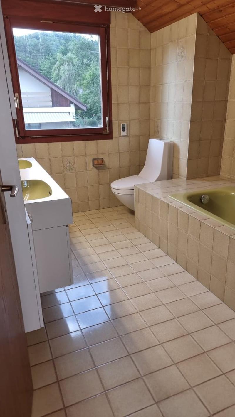 Bathroom with beige tiles, a toilet, a sink, and a bathtub, featuring a large window with a view of greenery.