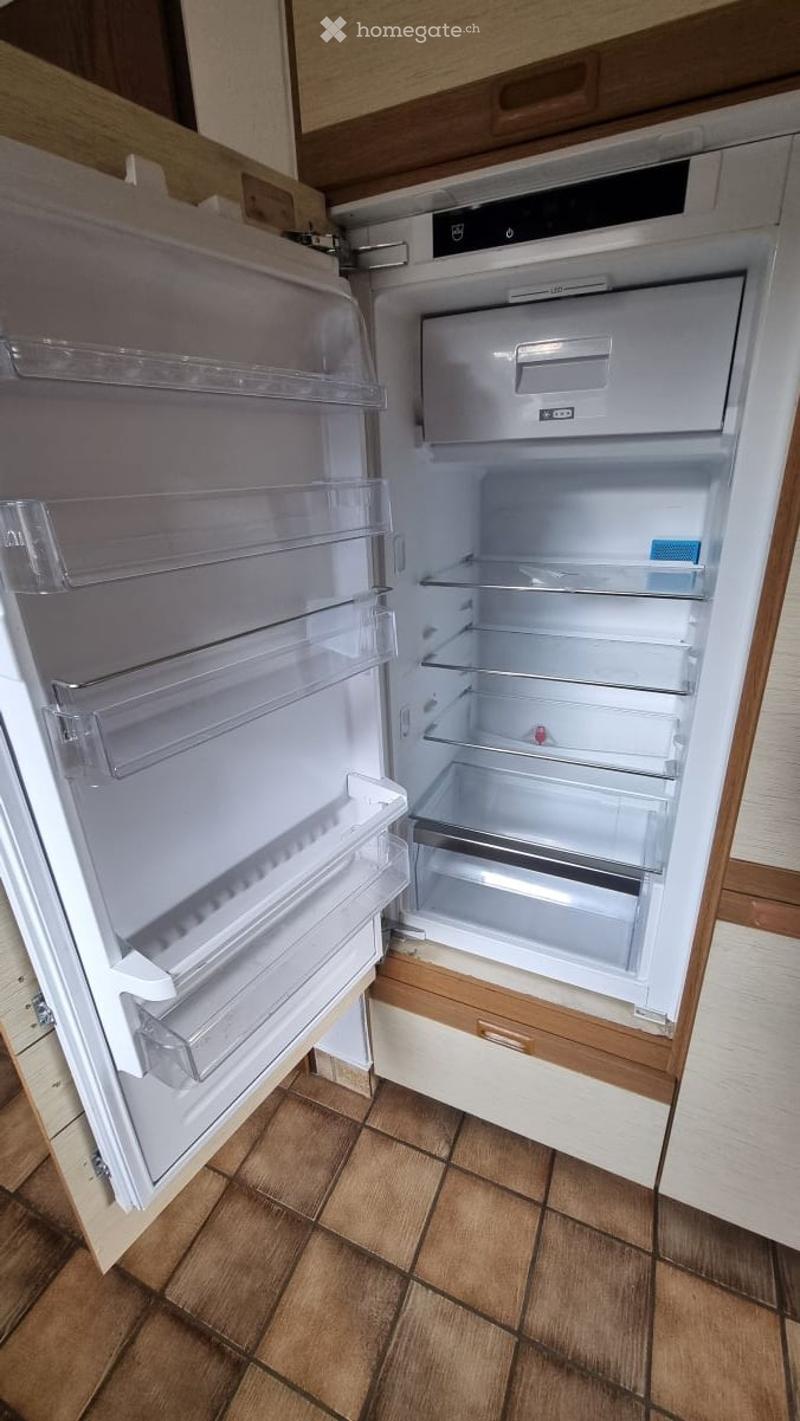 Open refrigerator with multiple shelves and compartments, located in a kitchen with wooden cabinets and tiled flooring.