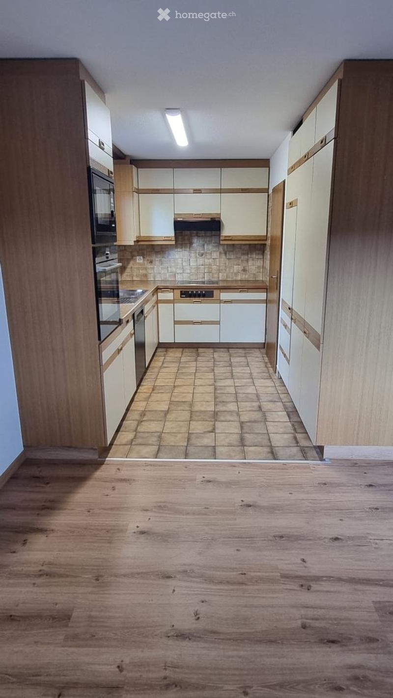 Empty kitchen with wooden cabinets, tiled backsplash, and wooden floor. No appliances or furniture present.