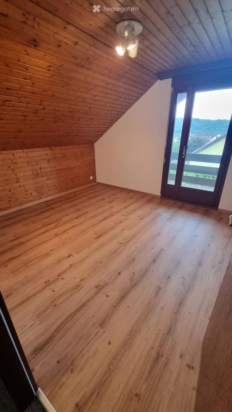Empty attic room with wooden walls and floor, skylight, and large window offering a view.