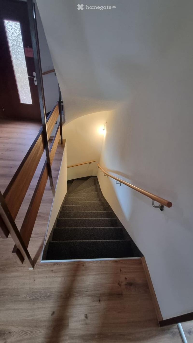 Spiral staircase with wooden handrails and carpeted steps, leading upwards in a modern interior setting.