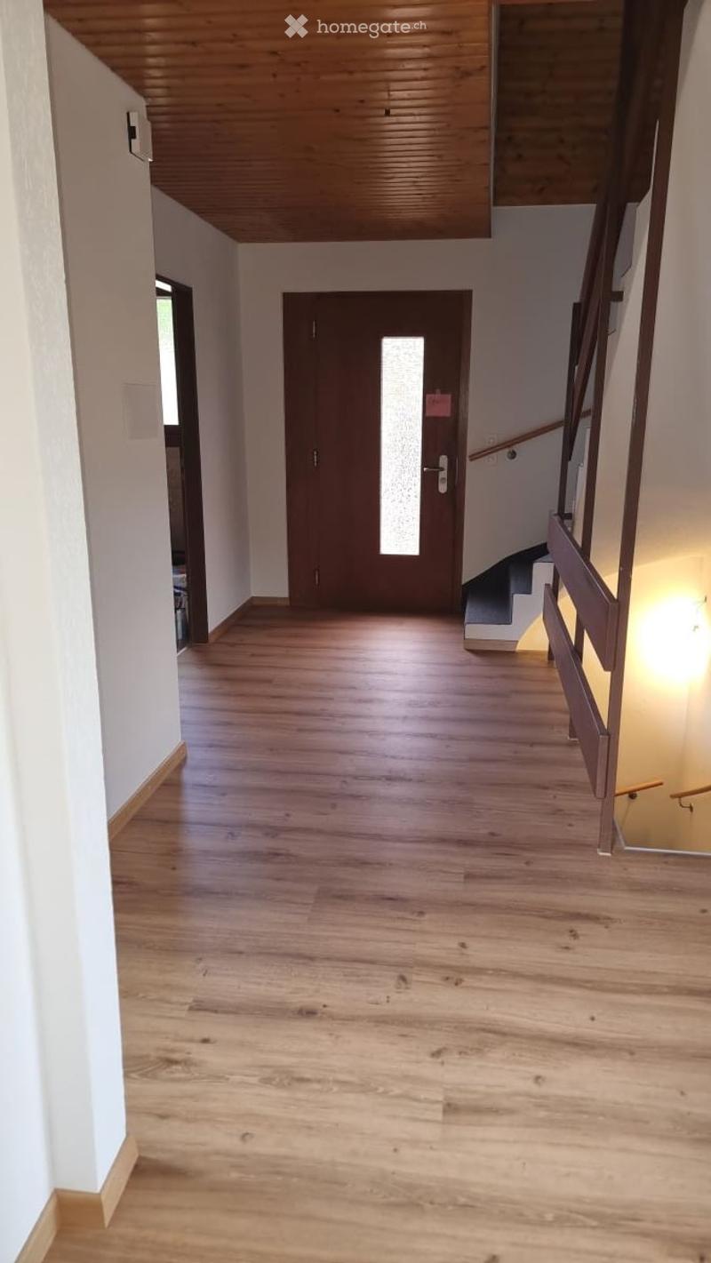 Empty hallway with wooden flooring, white walls, and a staircase leading upwards.