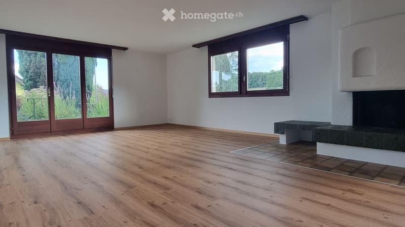 Empty room with wooden flooring, large windows, and a fireplace with a stone surround.