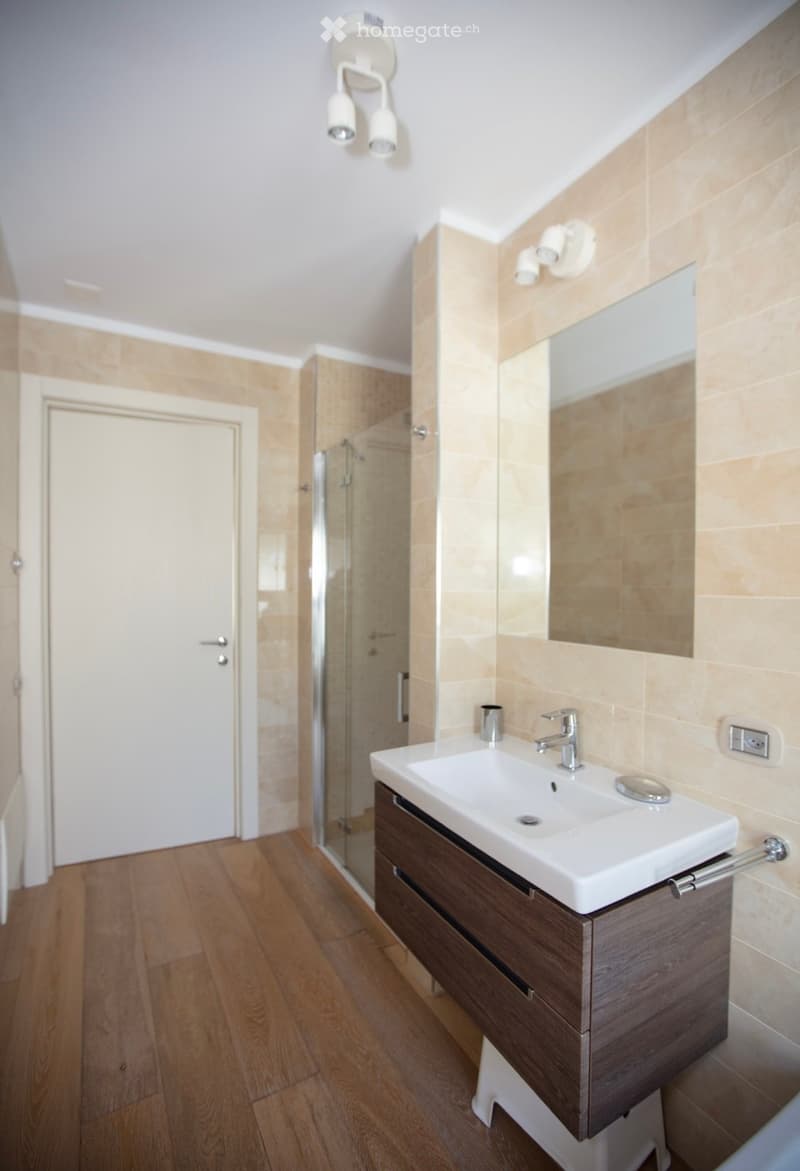 modern bathroom with wooden floor, white walls, glass shower, white sink, mirror, wooden cabinet, silver faucet