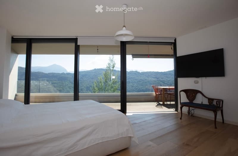 bedroom with large windows, balcony, wooden floor, bed, bench, TV, outdoor table and chairs