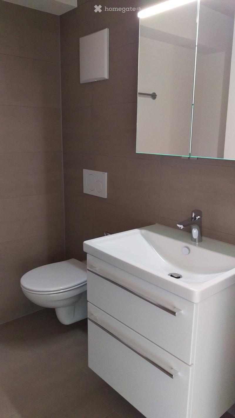 A small, modern bathroom with white sink, white toilet, and mirror mounted on the wall.