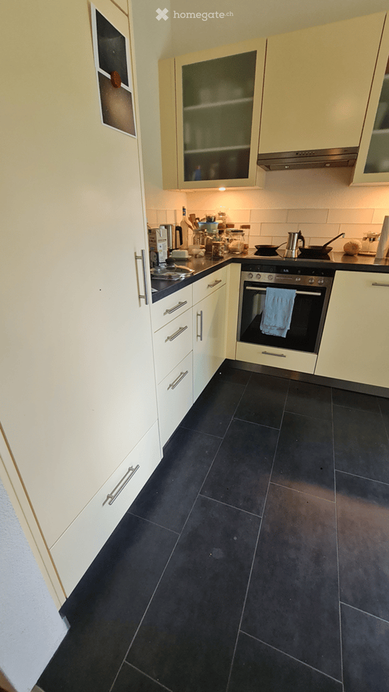 Modern kitchen with white cabinets, black tiled floor, stainless steel oven, and countertop with various kitchen items.