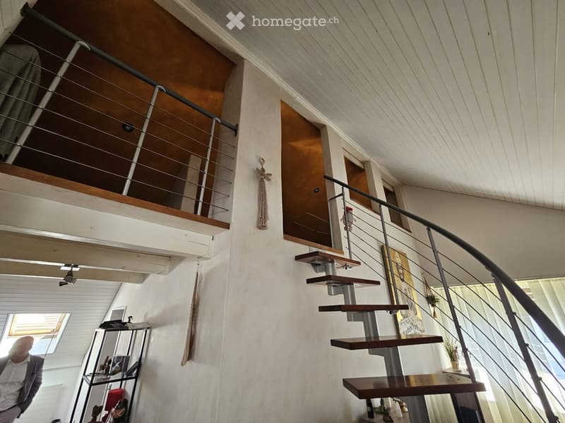 Modern interior staircase with wooden steps and metal railings, leading to an upper level with exposed wooden beams and white walls.