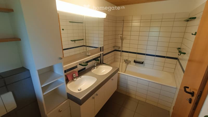 Bathroom with white tiles, double sink, bathtub, mirror, and built-in cabinet with shelves.