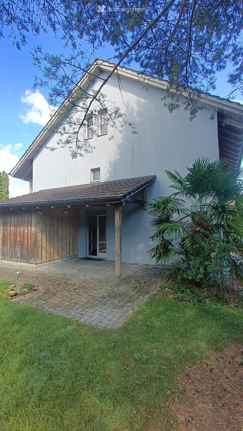 Two-story white house with a tiled roof, garage, and small garden area with palm trees and grass.
