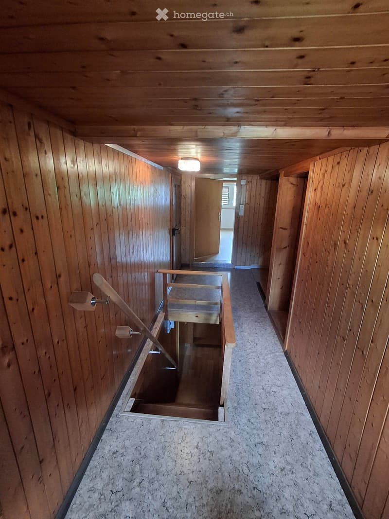 Wooden-paneled hallway with a staircase leading upwards, featuring a wooden railing and light fixture.