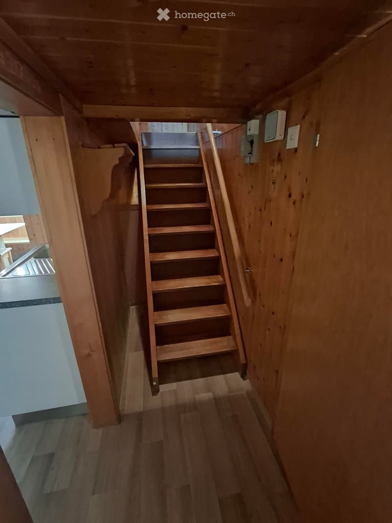 Wooden staircase leading upwards with wooden railings and walls, wooden flooring, and electrical outlets visible on the right wall.