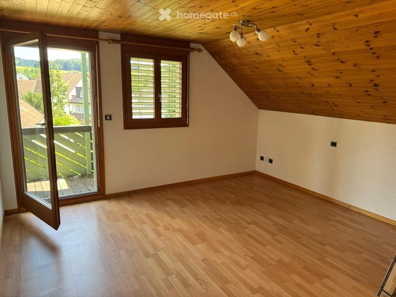 Empty room with wooden flooring, white walls, wooden ceiling, large window with blinds, and sliding glass door leading to a balcony.