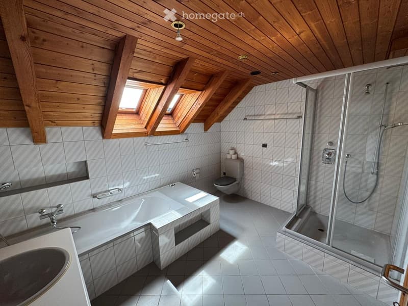 Bathroom with a wooden slanted ceiling, skylight windows, tiled walls, bathtub, toilet, sink, and a glass-enclosed shower.