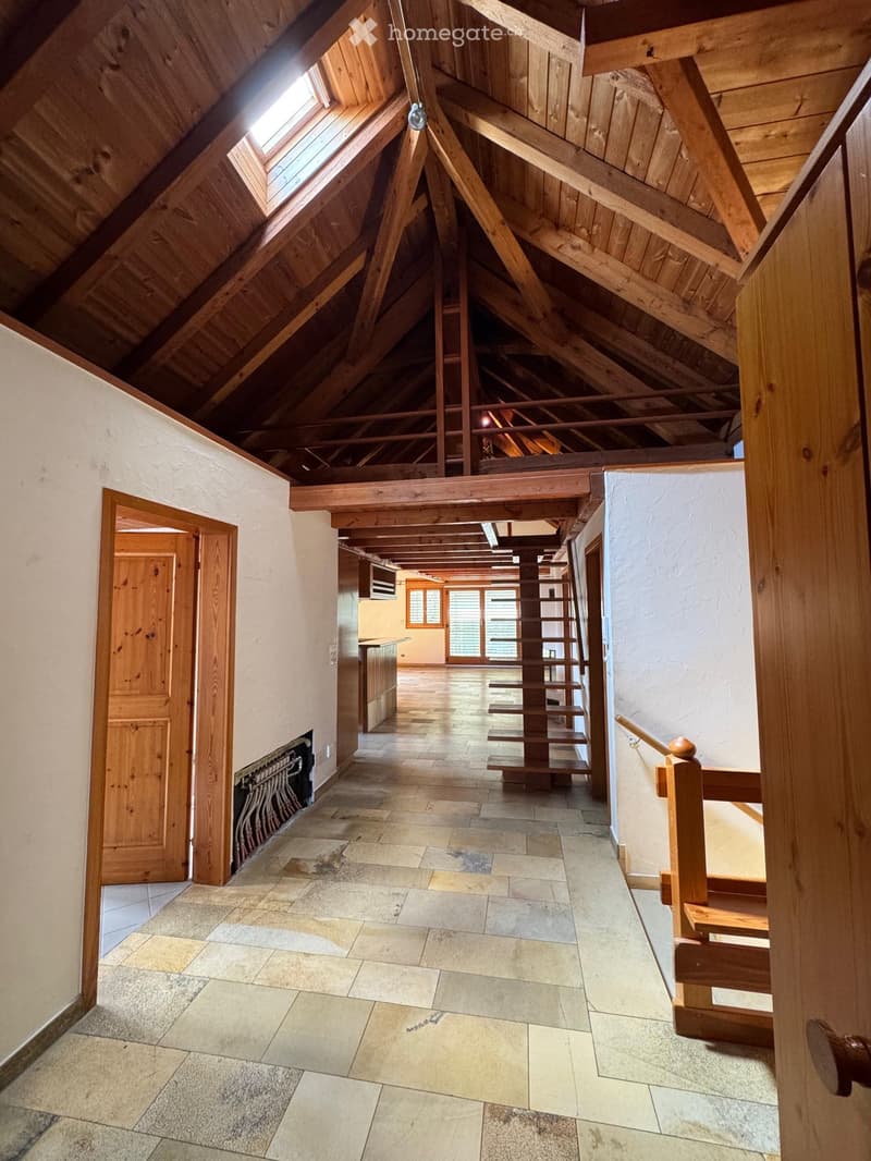 Spacious hallway with exposed wooden beams, stone tiled floor, wooden staircase, and multiple doors leading to other rooms.